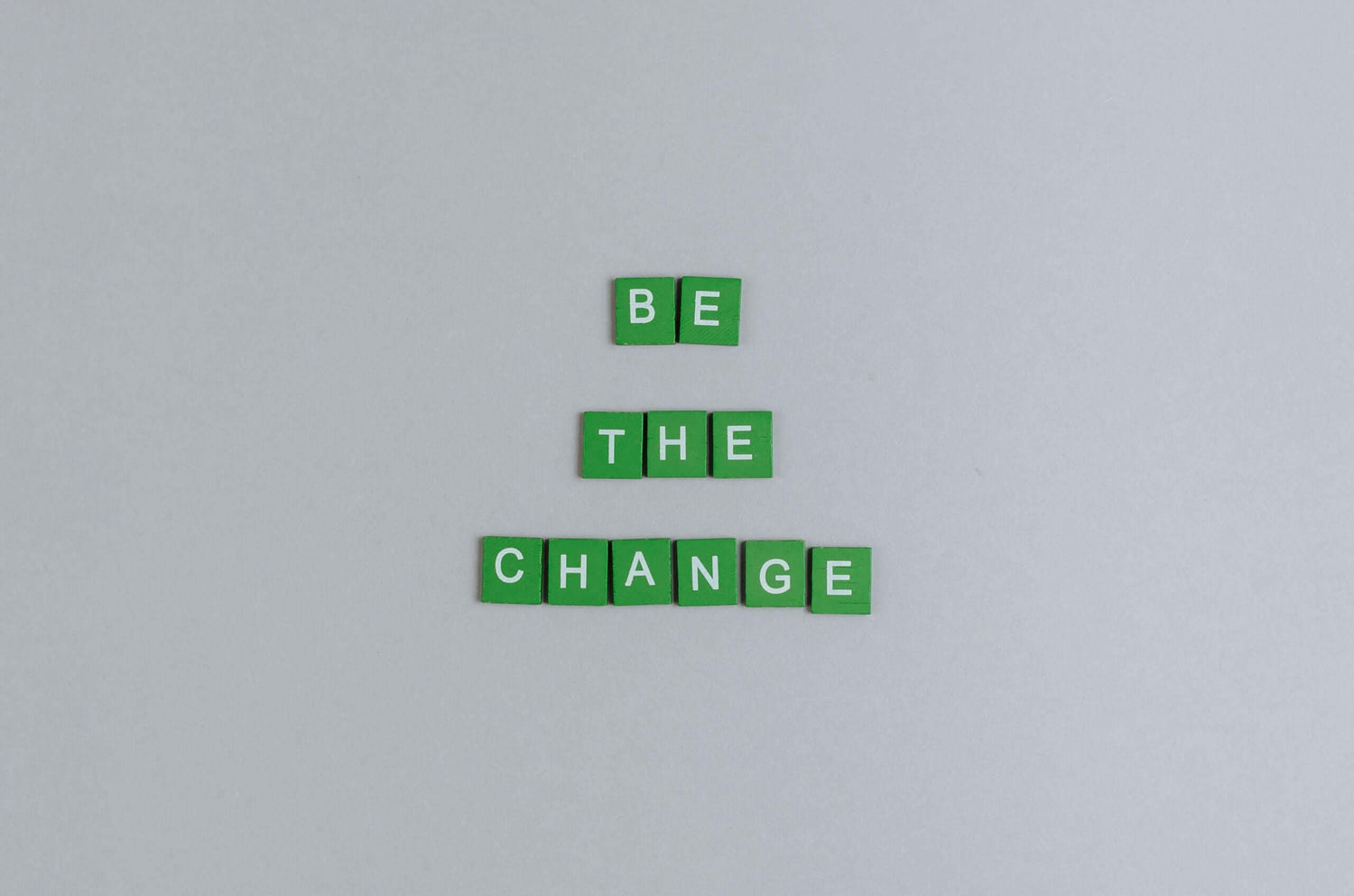 כיתוב "BE THE CHANGE" על רקע אפור עם אותיות ירוקות.